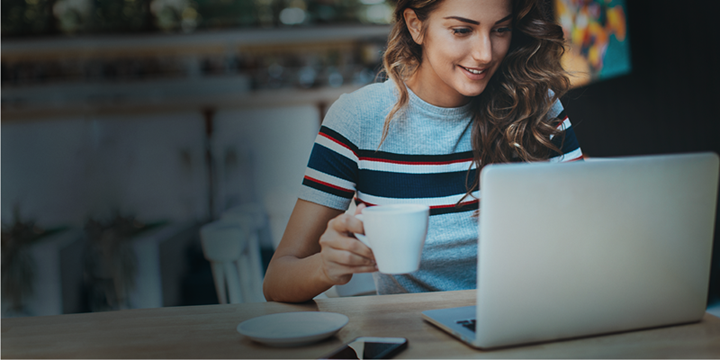 a woman holding a cup of coffee while using a laptop